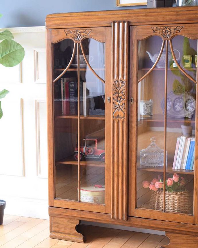 アンティークのキャビネット　アンティーク家具　イギリスアンティークの収納家具、お花の彫刻入りのブックケース（キャビネット）。ガラス越しに中をのぞいてみると･･･アンティークのガラスを通して中に入っているものを見ると、なんだかちょっと高級に見えるんです。(k-2319-f)