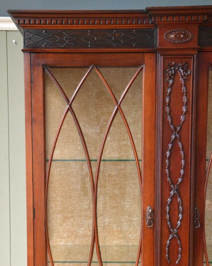 アンティークのキャビネット　アンティーク家具　アンティークの大きな英国家具、リボンの装飾が優雅なガラスキャビネット（ショーケース）。いろんな場所にこだわり彫のデザインもいろいろです。(q-1677-f)