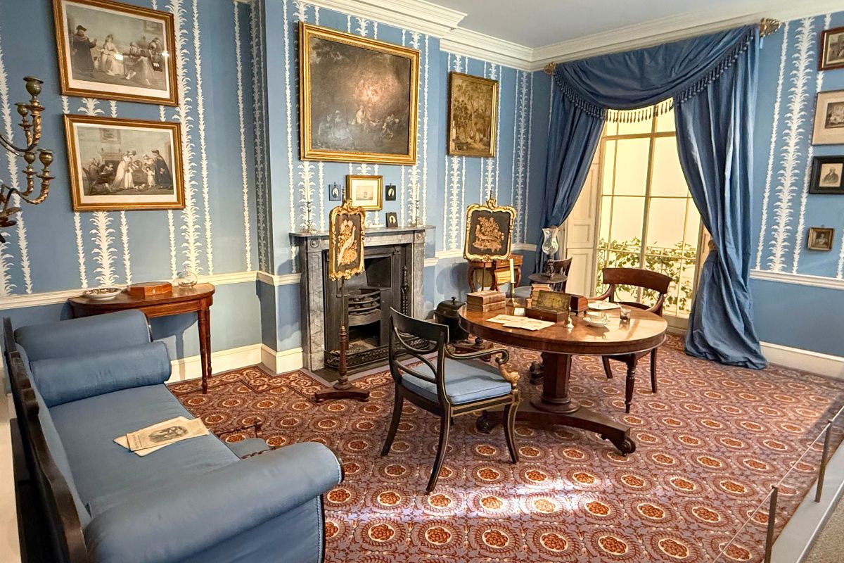 1830年のドローイングルーム。青い壁紙、円卓、ソファのある部屋全景