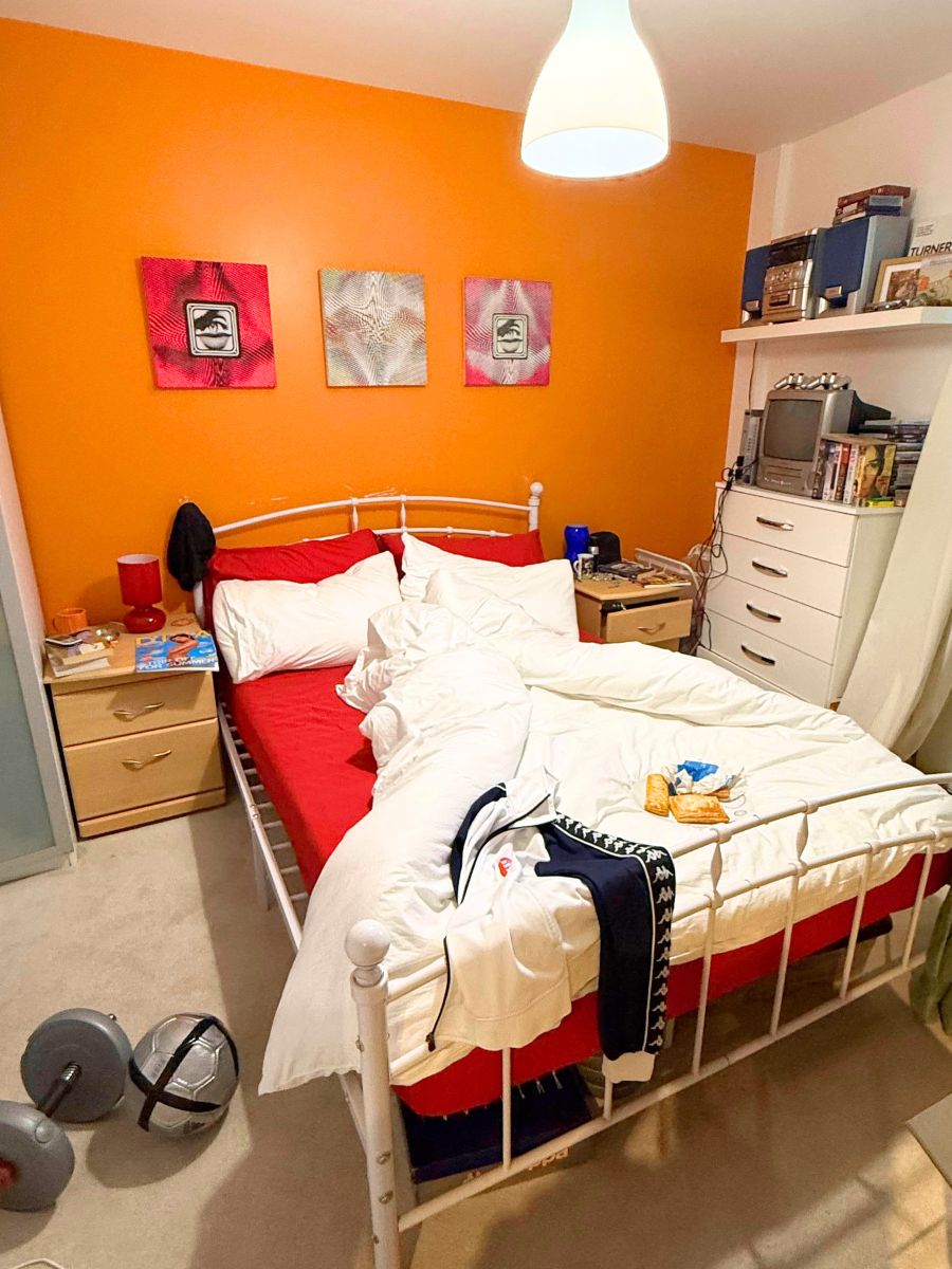 鮮やかなオレンジ色の壁のベッドルーム。散らかったベッドと個人的なアイテム